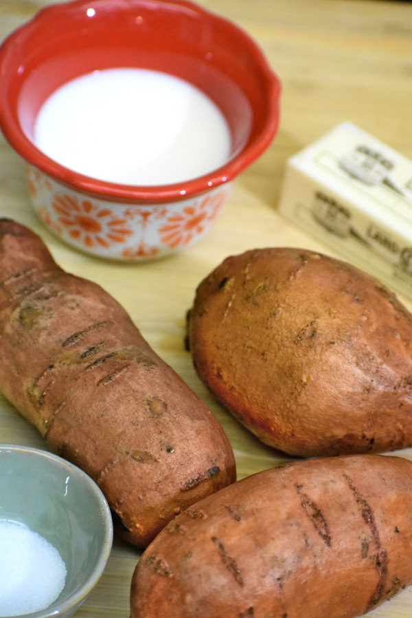 三个红薯，黄油，盐和一碗牛奶放在竹砧板上