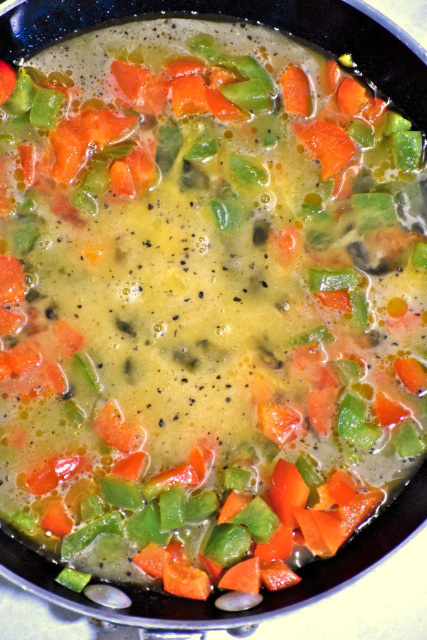 在不粘锅里，把生炒鸡蛋和红色和绿色甜椒块混合在一起