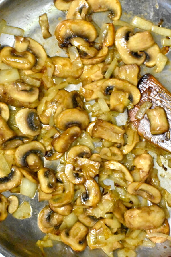 洋葱和蘑菇sautéing在不锈钢煎锅。
