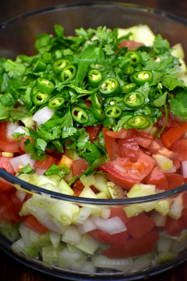 将切碎的西红柿、黄瓜和洋葱放入玻璃碗中，浇上香菜和墨西哥辣椒丁