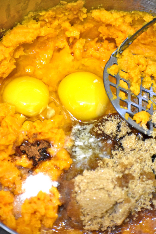 把红薯泥放在一个大锅里，加红糖、肉桂、盐和两个打好的鸡蛋，旁边放捣碎器