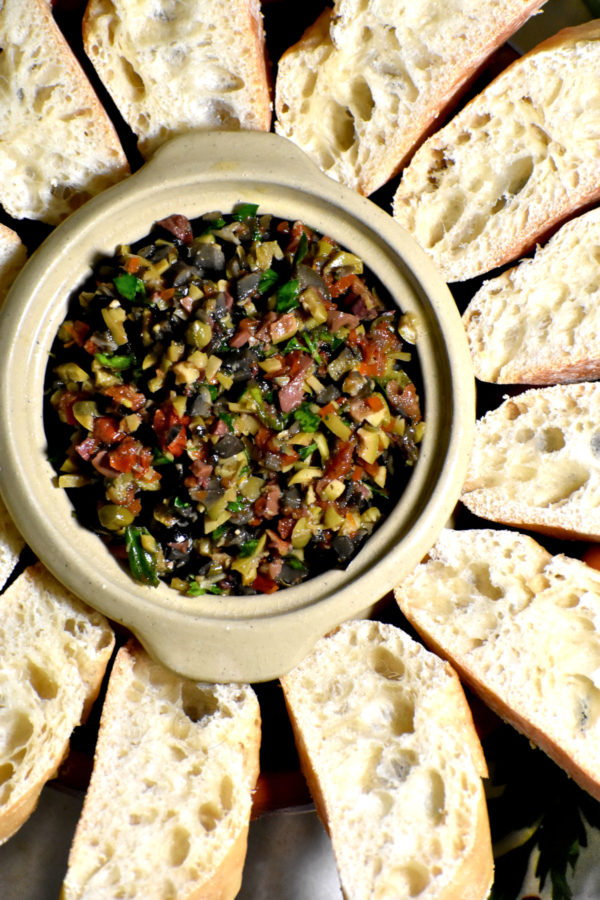 装满橄榄酱的小白碗，周围是切好的法棍面包。