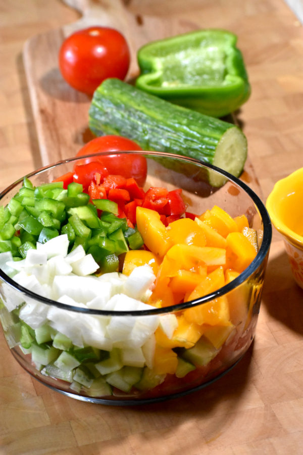 将番茄、辣椒、洋葱和黄瓜切碎，放入玻璃碗中