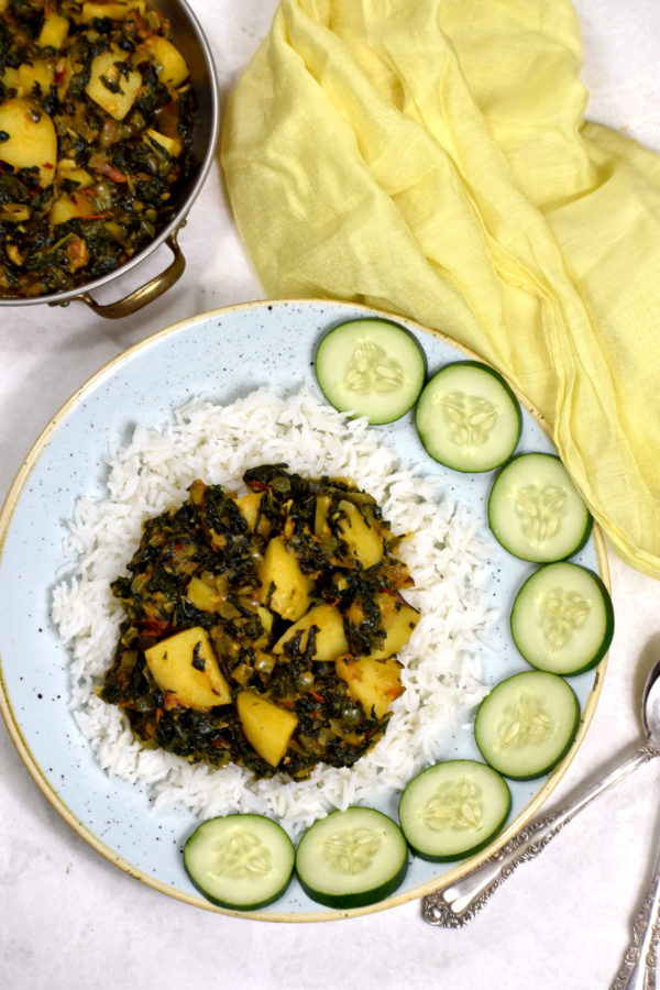 Aloo Palak摆放在一层白米饭上，点缀着黄瓜片。