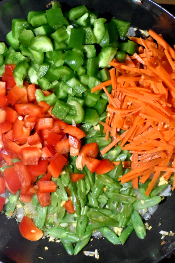 将切好的灯笼椒、胡萝卜和青豆放入锅中。